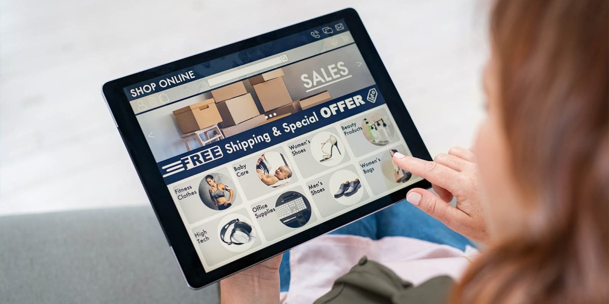 Back view of mature woman doing shopping online on website with digital tablet at home. Top view of woman with red hair relaxing on sofa while shopping online on ecommerce website. Rear view of girl hand touching screen while selecting product on e-commerce portal.